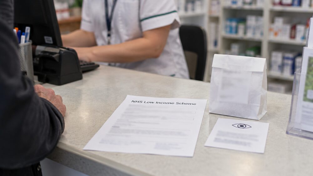 Prescription glasses in a case beside a white pharmacy bag on a bathroom shelf.