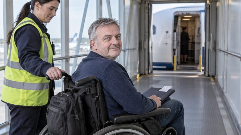 An airport staff member assisting a wheelchair user through the terminal
