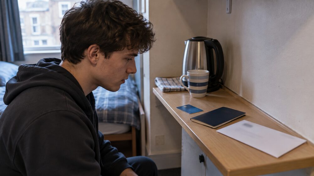 A debit card, ID booklet and envelope lie on a narrow bedsit shelf beside a kettle.