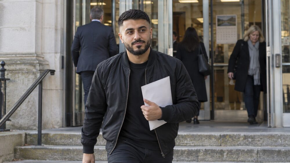 A young man holds an envelope on the steps of a county court entrance.