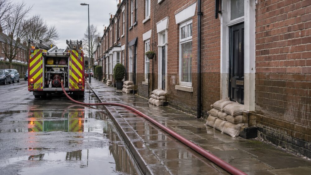 A fire service pump stands on a flooded street with sandbags against terraced house doors.