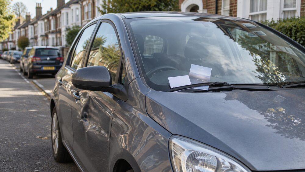 A business card and folded leaflet tucked under the wiper of a dented parked car.