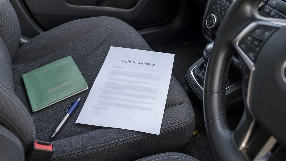 A sealed envelope lies unopened on a doormat inside a front door in morning light.