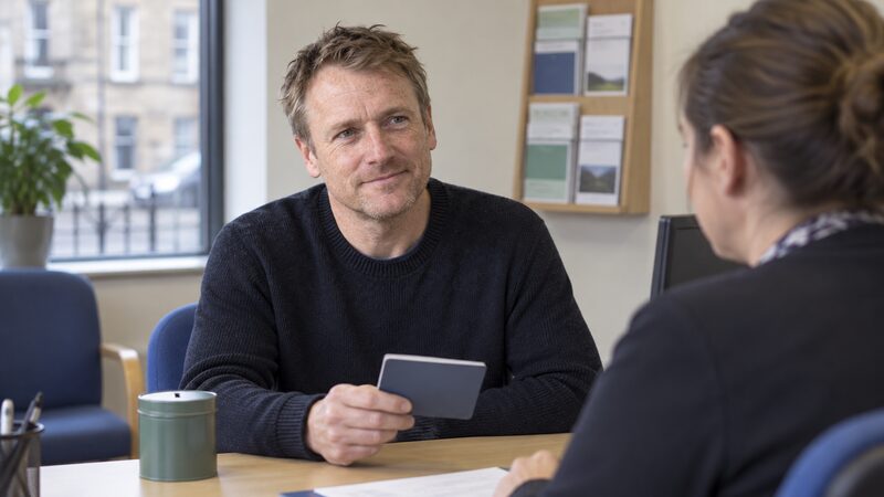 A man sits at a desk in a credit union office holding a passbook.
