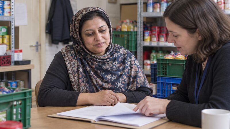 A woman sits with an adviser over a folder of papers in a shop back room.